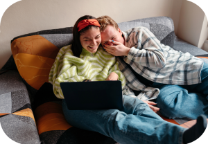 Jente og gutt ler og koser seg sammen foran en PC.