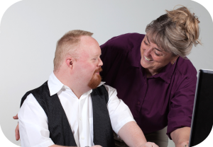 Smilende kvinne snakker med mann som jobber med sin PC.