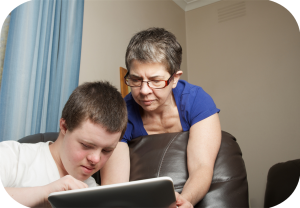 Eldre kvinne ser på PCn sammen med en ung mann.
