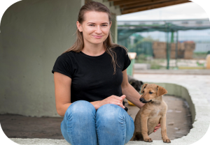 Ung kvinne med en liten hund sitter ute.